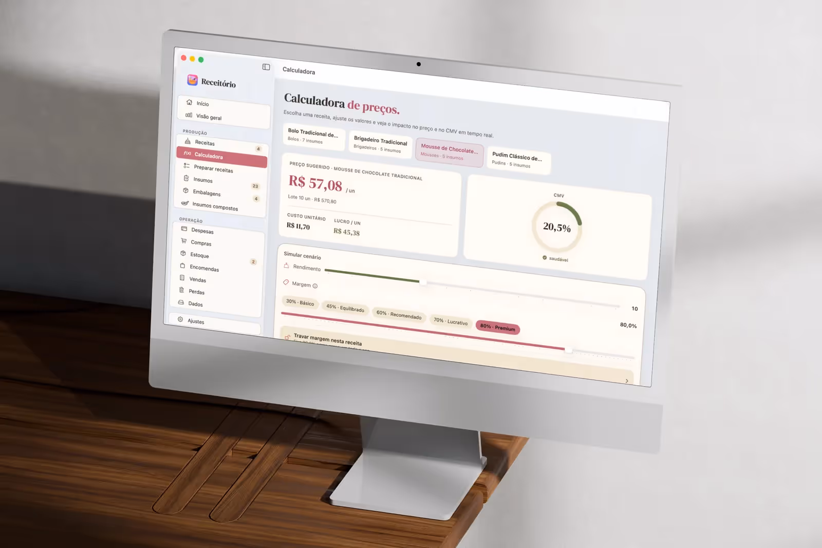 iMac numa escrivaninha de madeira com o Receitório aberto na Calculadora de preços e a sidebar da confeitaria