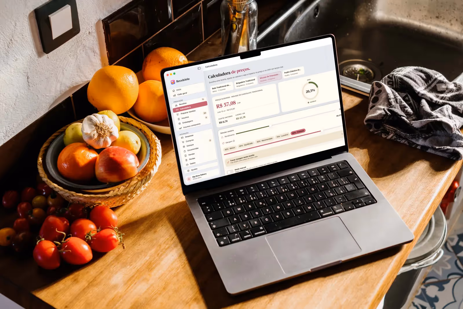 MacBook numa bancada de madeira ao lado de frutas e tomates, com a Calculadora de preços do Receitório aberta